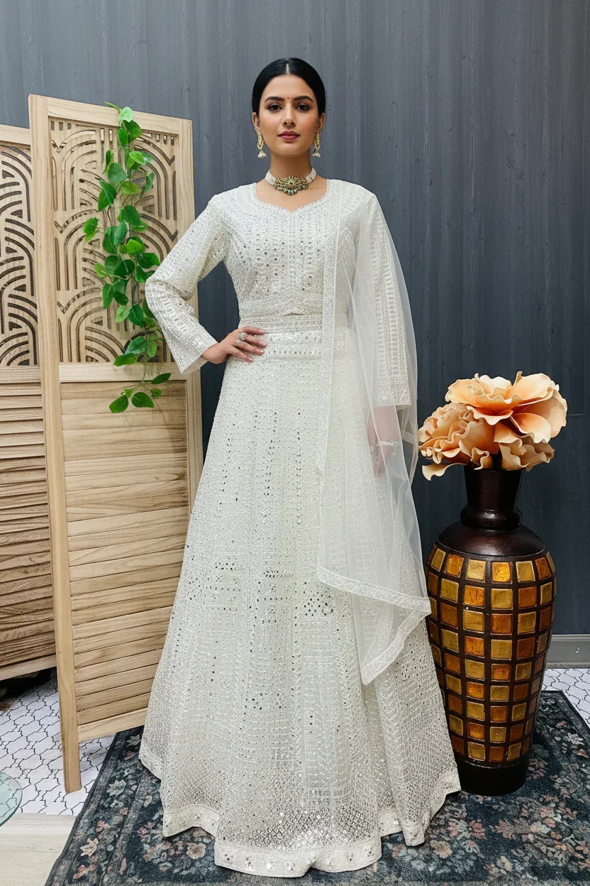 Woman wearing elegant white Indian ethnic lehenga with intricate embroidery and matching sheer dupatta, posing indoors