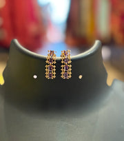 Gold earrings with purple rectangular gemstones displayed on black stand at Anandi Fashions boutique