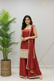 Woman wearing red Indian ethnic suit with embroidered kurta, matching dupatta and palazzo pants, posing indoors