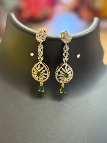Elegant gold and diamond Indian earrings with green gemstones displayed on black jewelry stand
