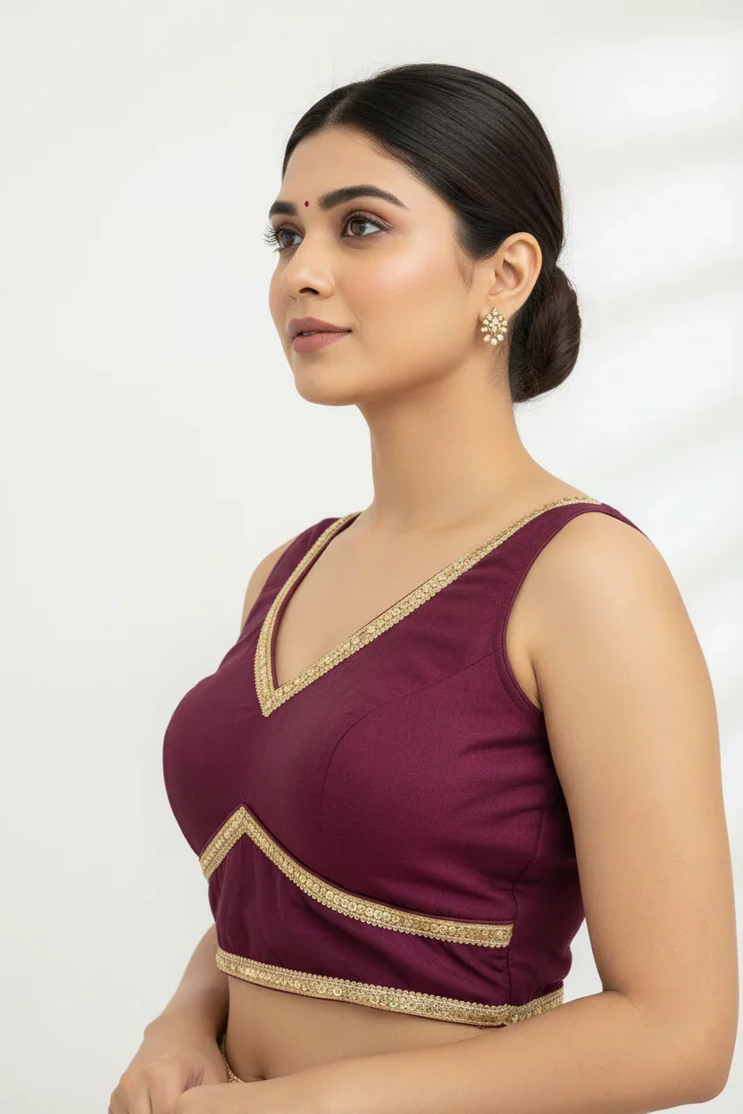 Woman wearing a sleeveless maroon Indian ethnic blouse with gold trim and pearl cluster earrings, styled hair