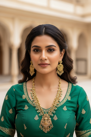 Indian woman in emerald green ethnic wear with intricate gold embroidery, wearing ornate gold necklace and matching earrings in traditional courtyard