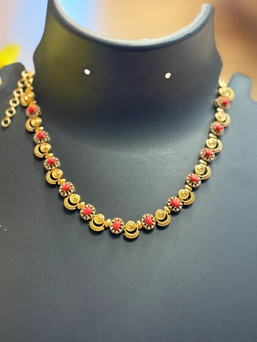 Gold necklace with alternating red stones and intricate gold floral designs displayed on black stand