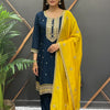 Woman in navy blue embroidered Indian ethnic wear with vibrant yellow dupatta, standing indoors near plant