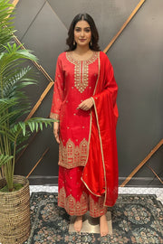 Woman in red embroidered Indian ethnic wear with matching dupatta standing indoors on a decorative rug