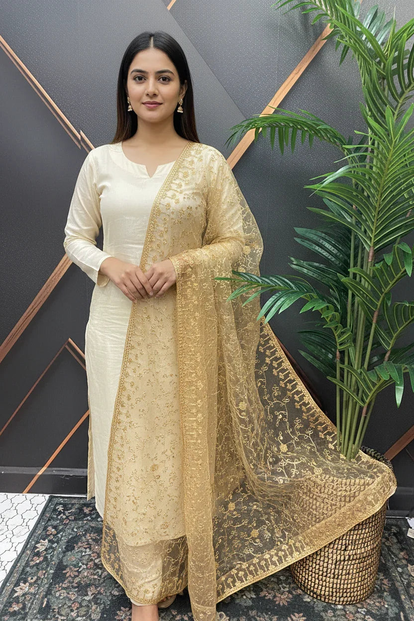 Woman wearing cream Indian ethnic wear with gold embroidered dupatta, posing indoors near green plant