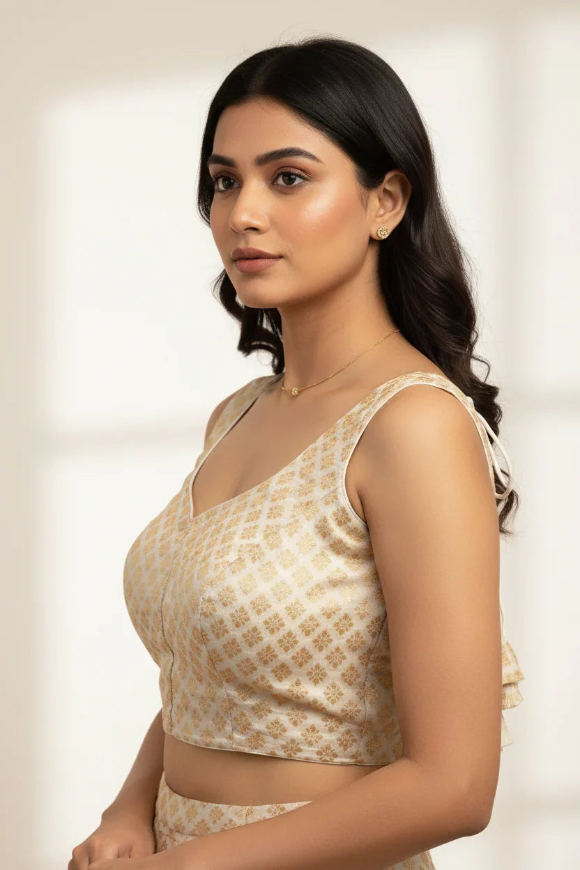Woman wearing beige and gold brocade Indian ethnic blouse with delicate earrings and necklace