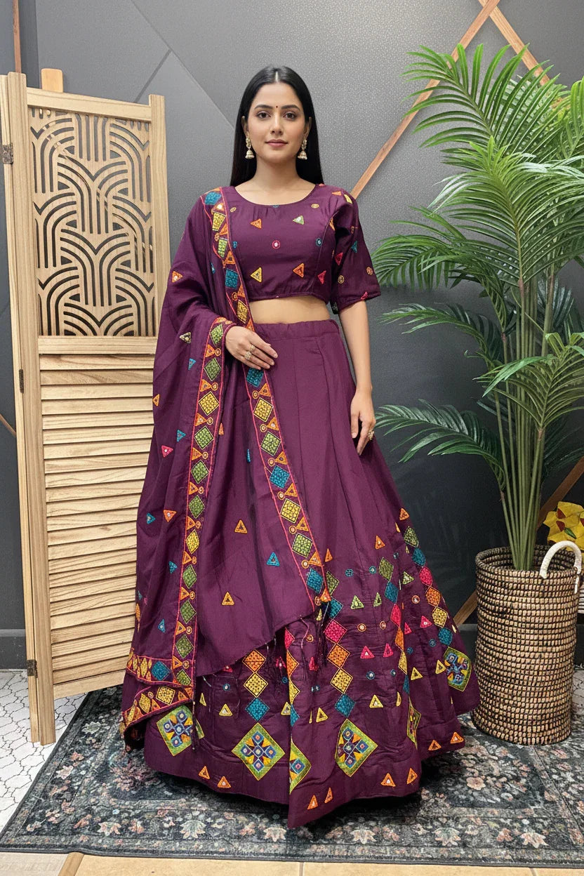 Woman in purple Indian ethnic lehenga with colorful geometric embroidery, standing indoors near plant and wooden screen