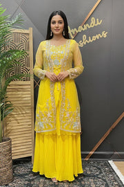 Woman in a yellow traditional outfit standing next to a plant with 'Brande Fashions' in the background.