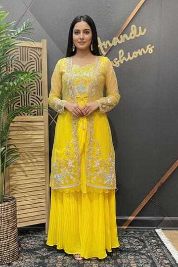 Woman in a yellow traditional outfit standing next to a plant with 'Brande Fashions' in the background.
