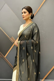 Woman wearing black embroidered saree with gold border and white blouse, styled with traditional jewelry, indoor studio setting