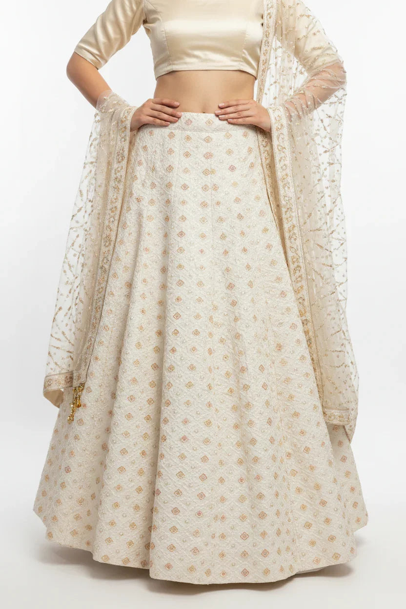 Woman wearing elegant beige Indian lehenga with gold and pink patterns and matching sheer embroidered dupatta