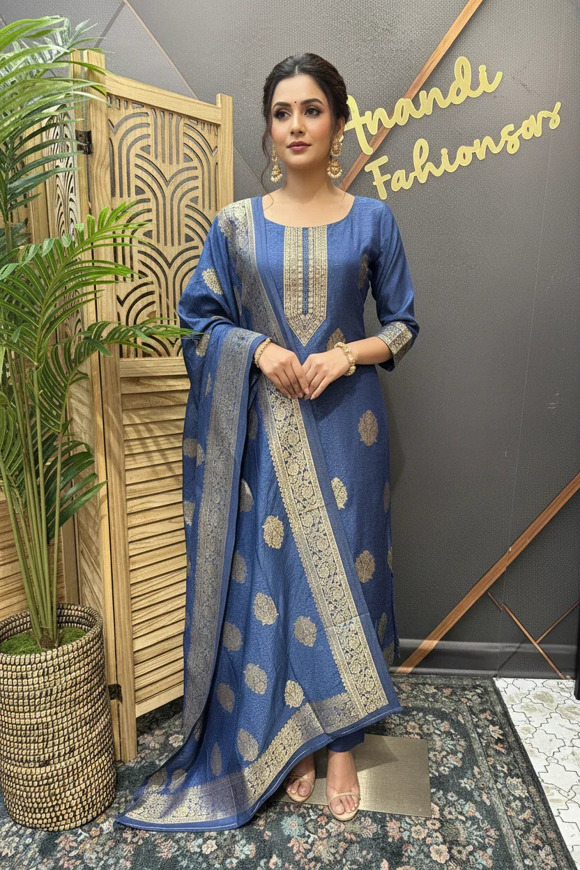Woman wearing blue ethnic Indian salwar kameez with gold motifs and dupatta, standing next to wooden screen and plant at Anandi Fashions