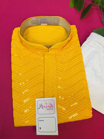 Folded yellow embroidered Indian ethnic kurta with tag on pink background beside white fabric and green leaves
