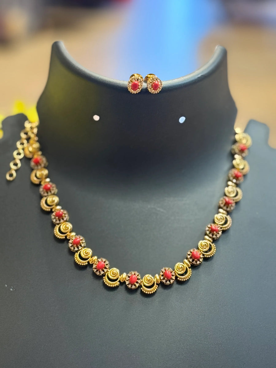 Gold and red stone Indian ethnic necklace and matching stud earrings displayed on black stand