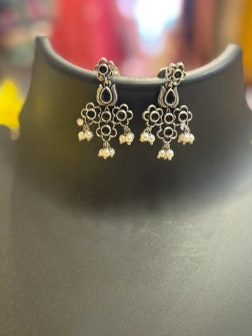 Silver-tone ethnic earrings with black stone floral designs and pearl drops on black display stand
