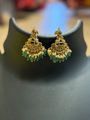 Gold-plated traditional Indian earrings with green and pearl beads, displayed on black stand