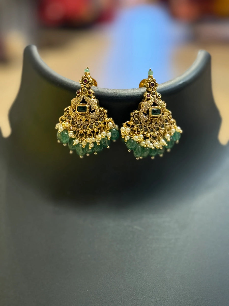 Gold-plated traditional Indian earrings with green and pearl beads, displayed on black stand