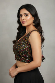 South Asian woman in black ethnic sleeveless blouse with floral embroidery and gold jhumka earrings against gray background