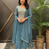 Woman in embroidered blue Indian lehenga, matching dupatta, standing indoors by decorative plant