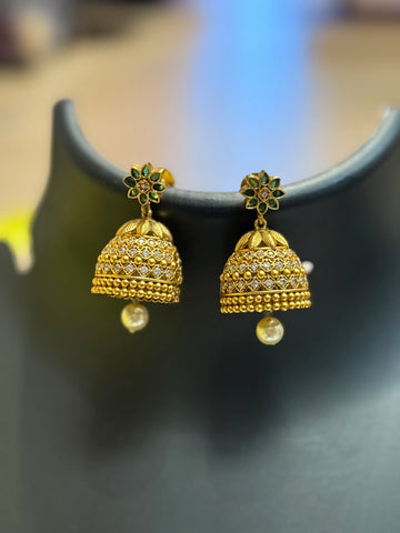 Pair of gold jhumka earrings with green enamel flower tops and pearl drops showcased on a black display
