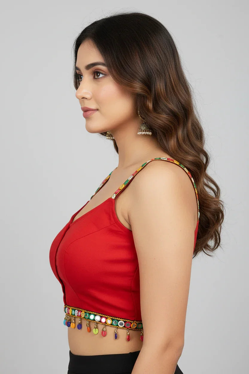 Side profile of a woman wearing red sleeveless ethnic crop top with mirror work and colorful embellishments, paired with jhumka earrings