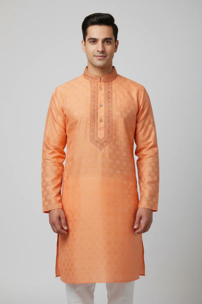 Man wearing peach orange embroidered Indian ethnic kurta with white pants on plain background