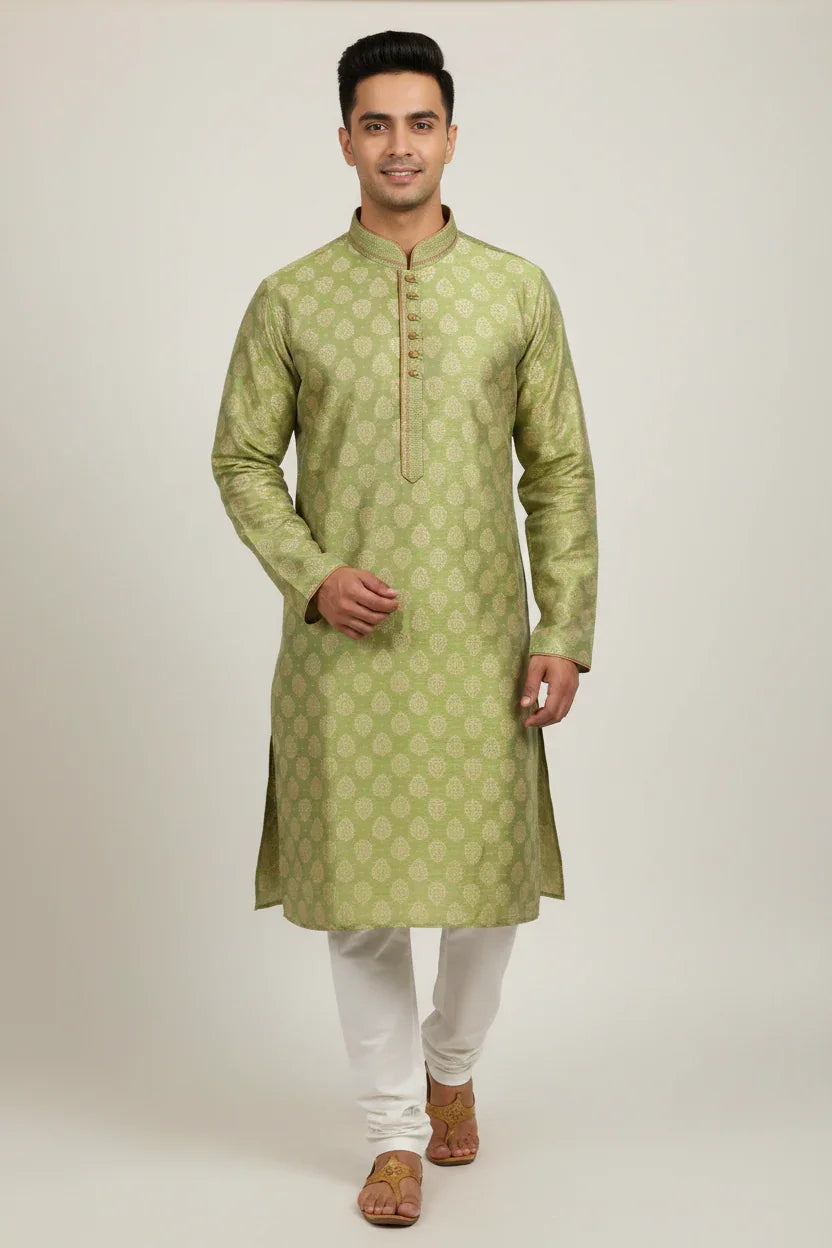 Man wearing green patterned Indian kurta with white churidar and brown sandals on plain background