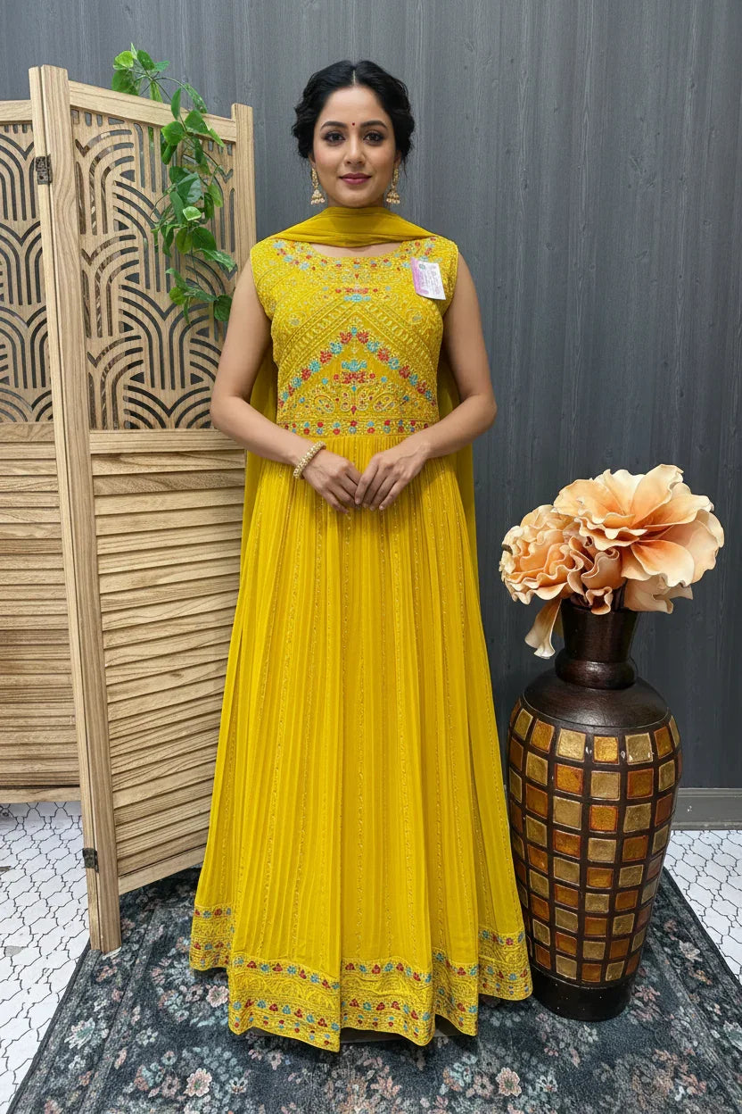 Woman in yellow embroidered Indian ethnic dress, standing indoors with decorative folding screen and vase