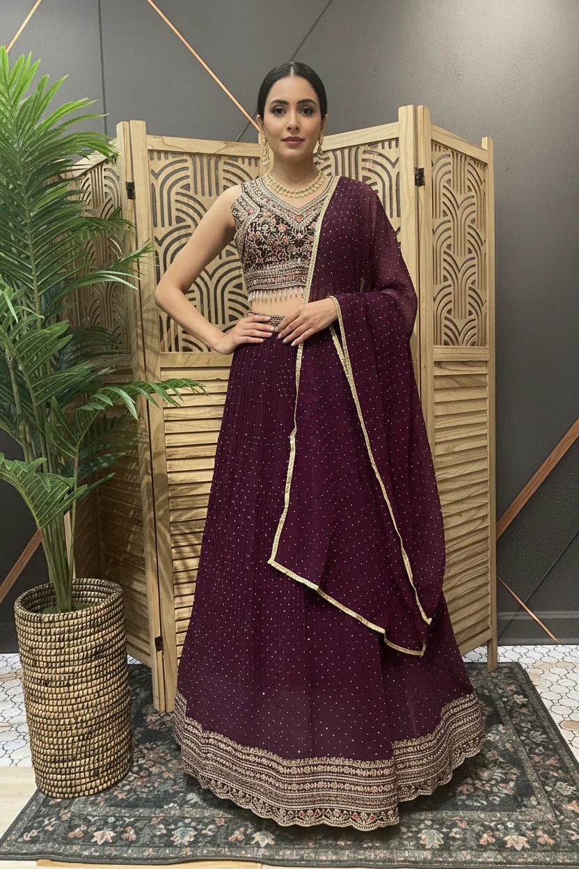 Woman in maroon embroidered Indian lehenga and dupatta standing indoors with a wooden screen and potted plant