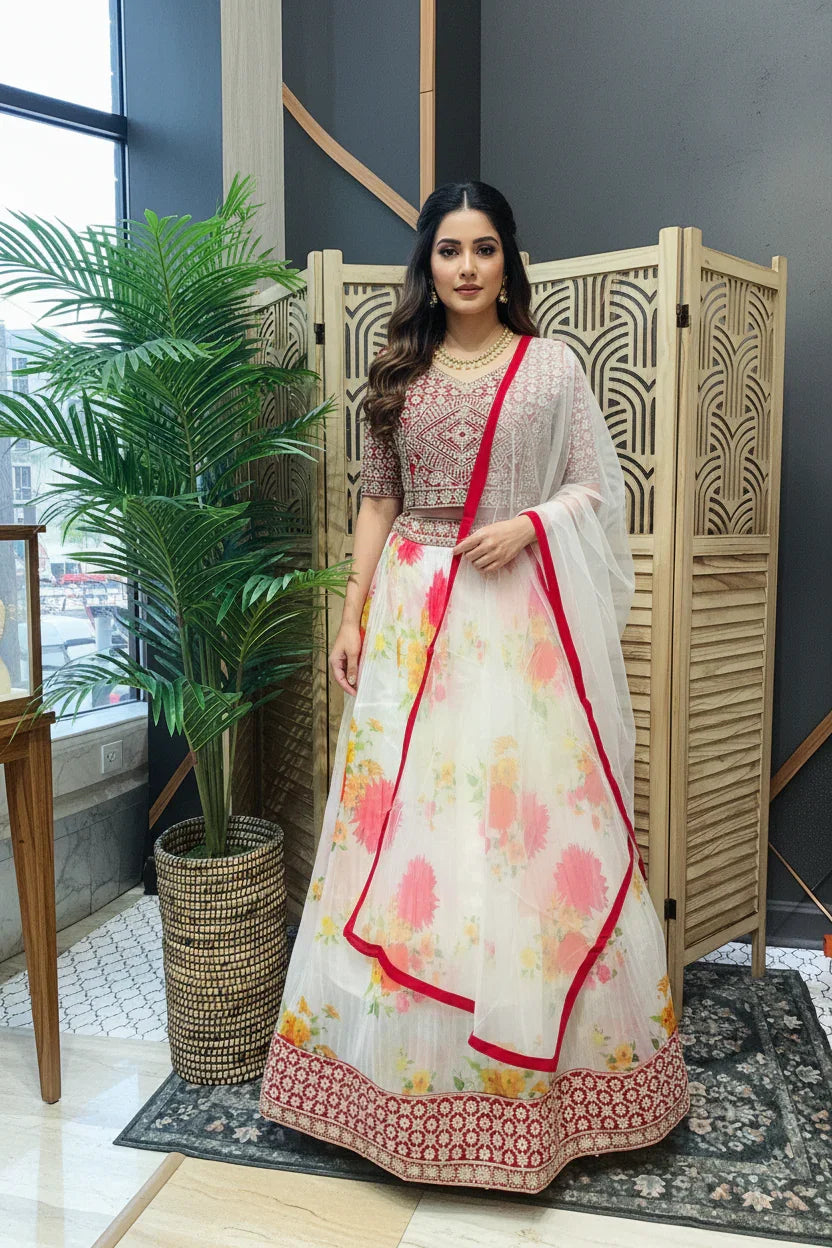Woman in embroidered red blouse and floral white lehenga with red border, posing indoors at Anandi Fashions