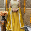 Woman in yellow embroidered Indian lehenga with matching dupatta and jewelry, standing indoors near a vase