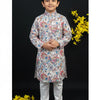 Young boy wearing colorful printed Indian kurta with white churidar and traditional sandals, yellow flowers background