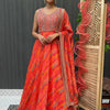 Woman wearing vibrant orange-pink embroidered Indian ethnic gown with matching dupatta, standing indoors