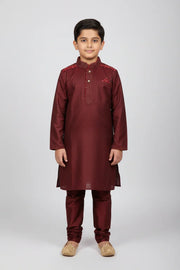 Young boy wearing maroon Indian ethnic kurta pajama with embroidery and golden traditional jutti shoes