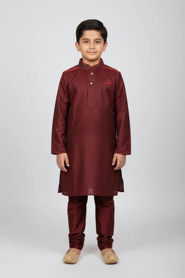 Young boy wearing maroon Indian ethnic kurta pajama with embroidery and golden traditional jutti shoes
