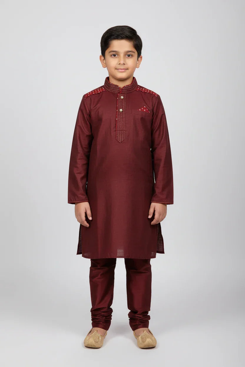 Young boy wearing maroon Indian ethnic kurta pajama with embroidery and golden traditional jutti shoes