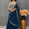 Woman wearing navy blue Indian ethnic lehenga with silver embroidery and matching dupatta, standing indoors beside decorative vase