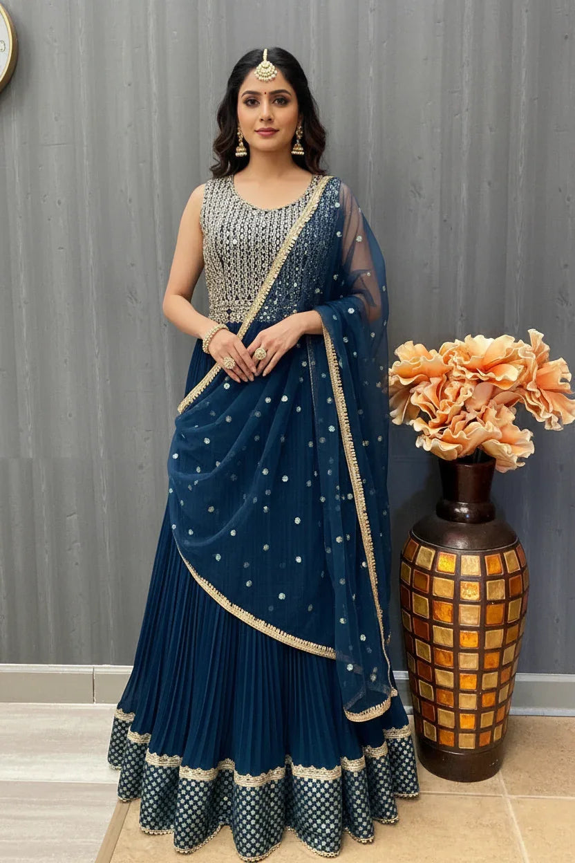 Woman wearing navy blue Indian ethnic lehenga with silver embroidery and matching dupatta, standing indoors beside decorative vase
