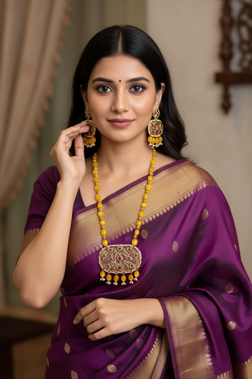 Woman in purple silk saree with gold border, wearing traditional yellow-beaded necklace and matching earrings