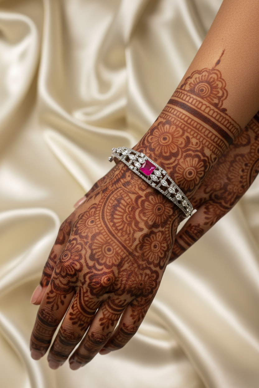 Hand with intricate brown mehndi design wearing silver bracelet with pink gemstone on cream satin fabric