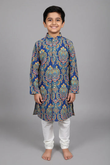 Smiling boy wearing blue floral patterned ethnic kurta with white churidar pants on gray background