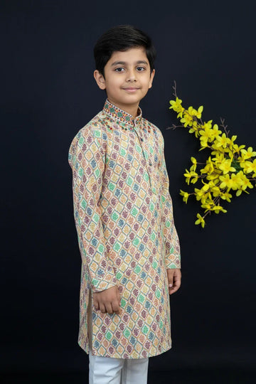Young boy in colorful printed kurta with white pants standing against black background with yellow floral decoration