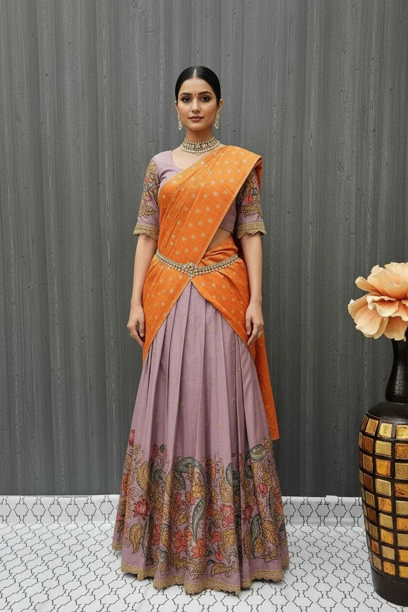 Woman in elegant purple lehenga with floral border and orange polka dot dupatta standing indoors