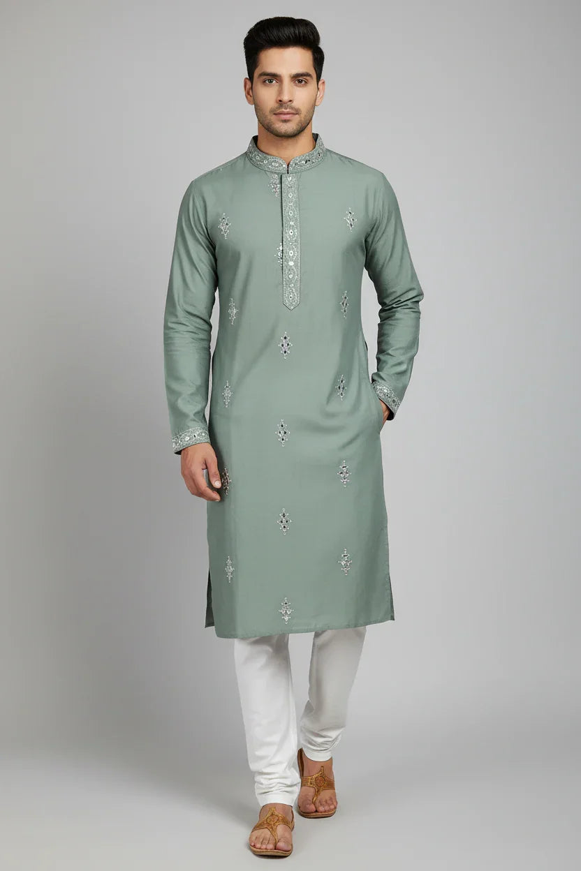 Man wearing sage green embroidered Indian kurta with white churidar and brown sandals