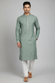 Man wearing sage green embroidered Indian kurta with white churidar and brown sandals