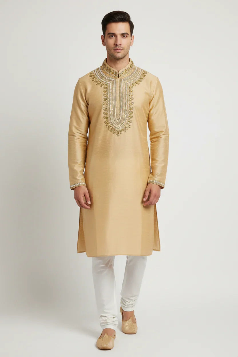 Man wearing beige embroidered Indian kurta with white churidar and traditional jutti shoes