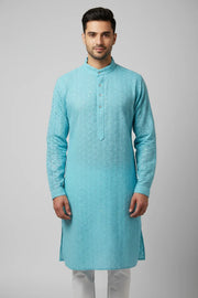 Man wearing sky blue embroidered Indian ethnic kurta with white churidar against gray background