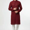 Man wearing a maroon embroidered Indian kurta with white churidar pants and brown sandals