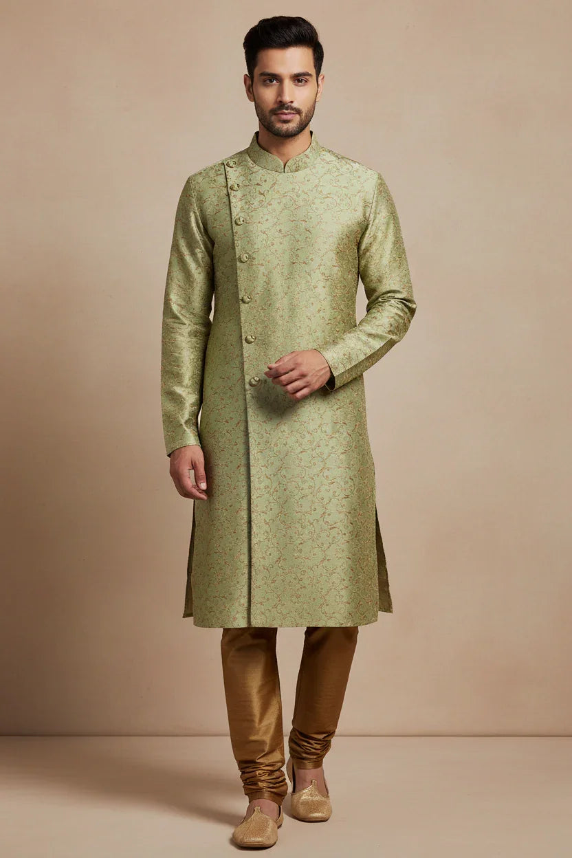 Man wearing a light green embroidered Indian sherwani with golden churidar pants and traditional jutti shoes
